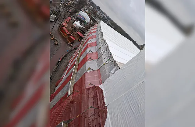 Blick von oben auf ein großflächiges weißes Wetterschutzdach mit rot-weißen Gerüstschutznetzen bei der Gebäudesanierung in Neumünster.
