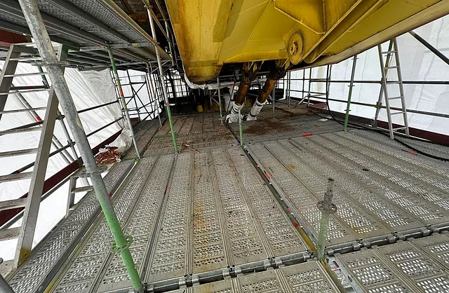 Industriegerüst mit Gitterrost-Arbeitsplattformen unter einer gelben Stahlkonstruktion innerhalb einer geschlossenen Schutzeinhausung.