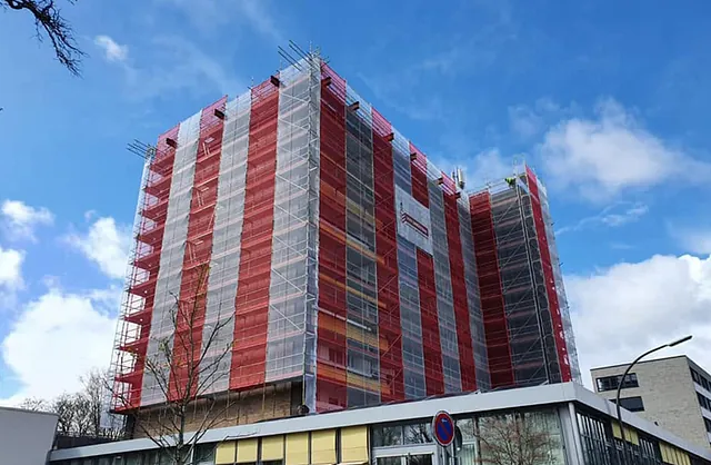 Mehrgeschossiges Wohngebäude mit rot-weißen Gerüstschutznetzen und Fassadengerüst von VVV Gerüstbau für Sanierungsarbeiten in Norderstedt.