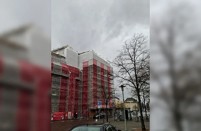 Mehrgeschossiges Fassadengerüst mit rot-weißen Schutznetzen an der Sparkasse Neumünster für sichere Bau- und Sanierungsarbeiten.