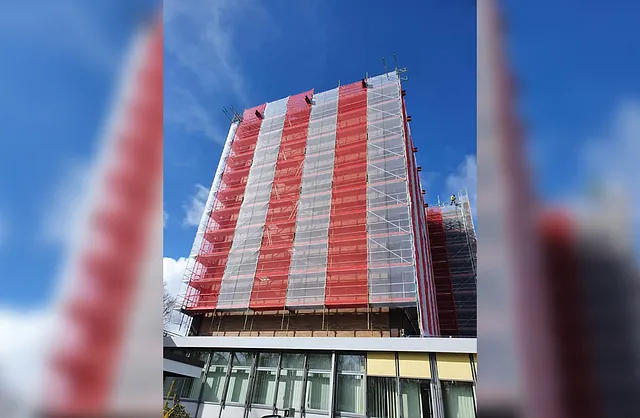 Hohes Fassadengerüst mit rot-weißer Schutznetzverkleidung an einem Wohngebäude in der Ochsenzollerstraße 144 in Norderstedt.