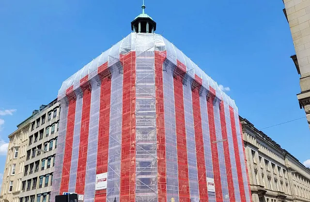 Mehrstöckiges Gebäude am Alstertor 16 in Hamburg mit Fassadengerüst und rot-weißen Schutznetzen von VVV Gerüstbau für Fassadensanierung und Bauarbeiten.