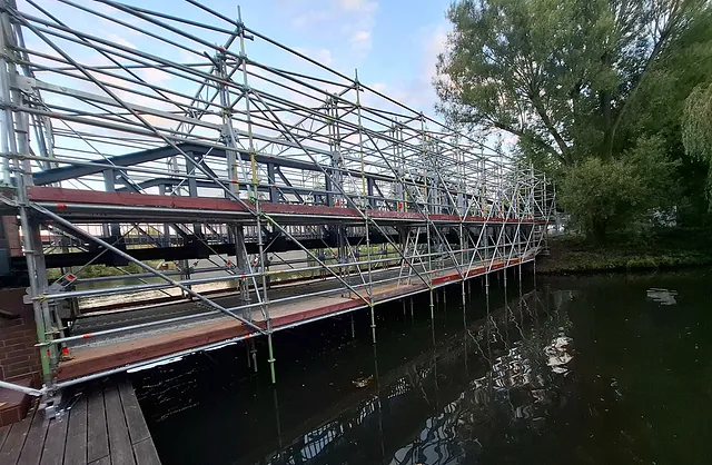 Seitliche Ansicht eines Spezialgerüsts mit mehreren Arbeitsebenen entlang einer Fußgängerbrücke über dem Wasser in Hamburg-Wilhelmsburg.