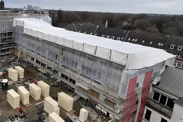 Großflächiges weißes Wetterschutzdach über einem eingerüsteten Gebäudekomplex zum Schutz vor Witterung bei Bau- und Sanierungsarbeiten in Neumünster.