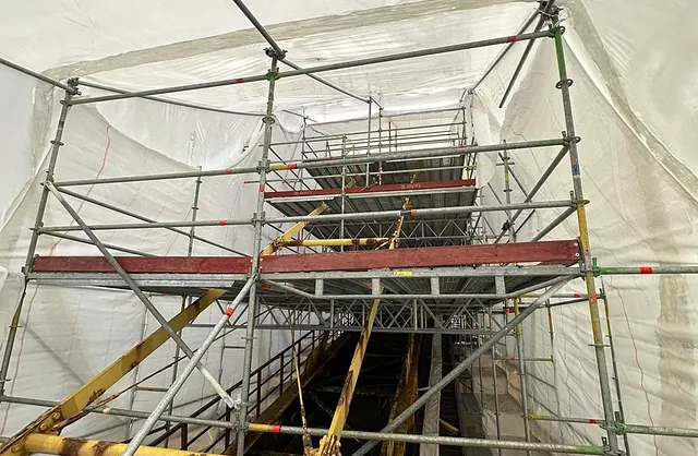 Komplexe Gerüstkonstruktion mit mehreren Arbeitsebenen und weißer Schutzeinhausung für industrielle Wartungs- und Instandhaltungsarbeiten.