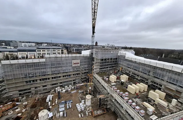 Luftaufnahme der Sparkasse Neumünster mit mehrgeschossigen Fassadengerüsten, Schutznetzen und Baukran für umfangreiche Bauarbeiten.