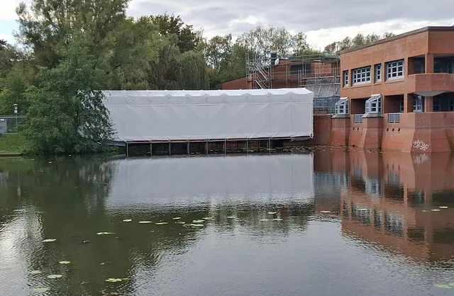Seitliche Ansicht einer vollständig eingehausten Fußgängerbrücke mit Spezialgerüst über einer Wasserfläche in Hamburg-Wilhelmsburg.