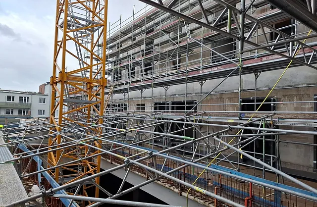 Mehrgeschossiges Fassadengerüst mit komplexer Stahlrohrkonstruktion und gelbem Baukran auf einer Großbaustelle in Hamburg-Barmbek.